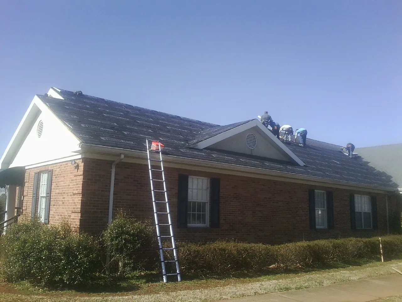 Crew tearing shingles off a brick ranch roof with a ladder set — Metal Roof Repair work by our crew in Wyoming