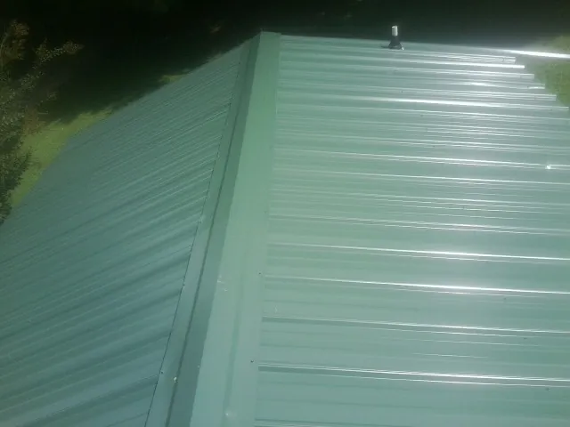 New green metal panels meeting at the ridge of a roof — Flat Roof Repair work by our crew in Wyoming