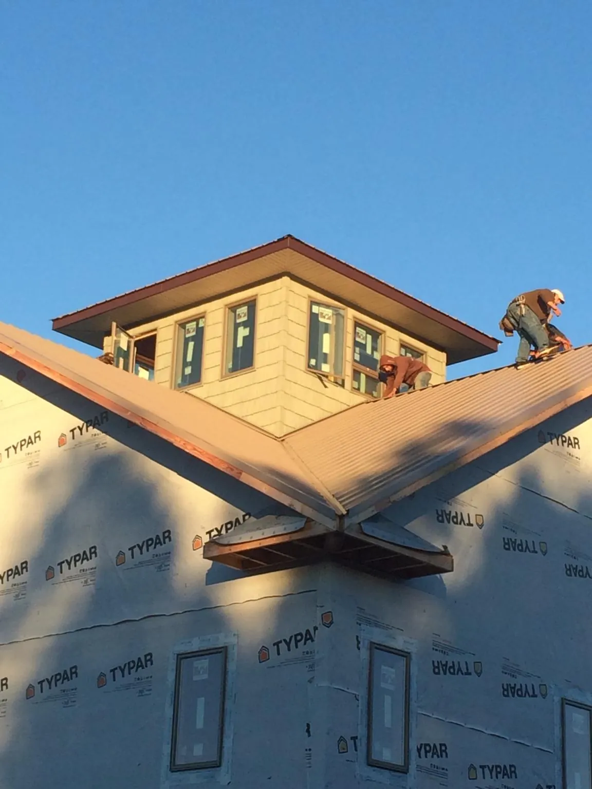 Roofers working around a rooftop cupola on a new metal roof at sunset — Roof Waterproofing in Wyoming by Roofing Brothers